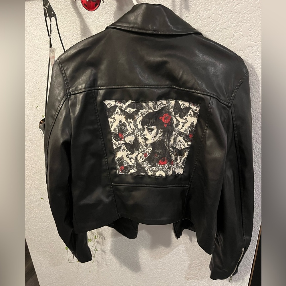 Black faux leather jacket with specialty fabric patch stitched on back.